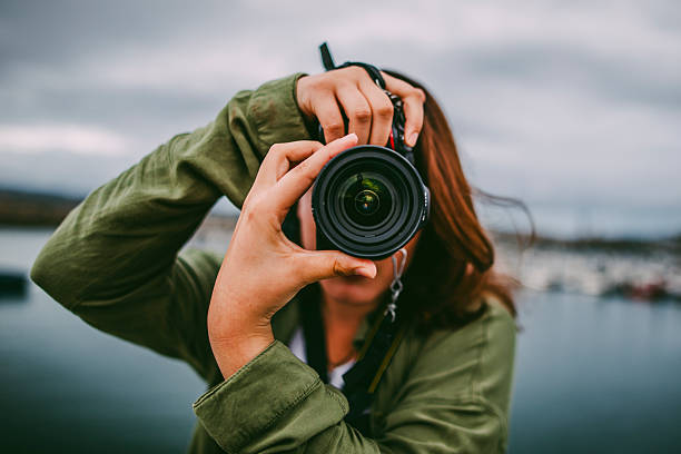 Photographer holding a digital camera near their face, focusing through the lens in an outdoor setting.